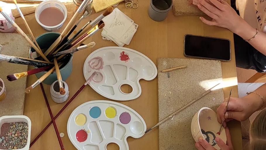 People painting pottery on wooden table.