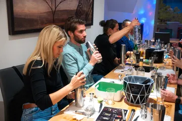 People shaking cocktail shakers at a bar.