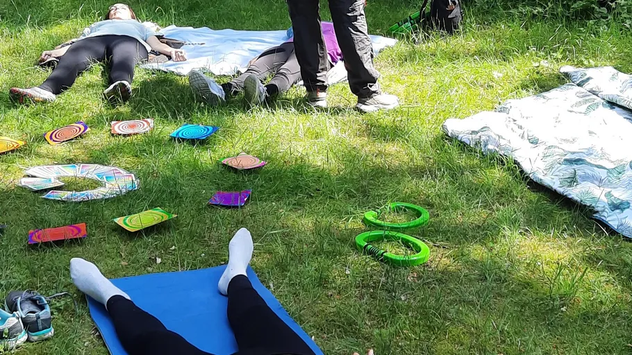 Personen liegen auf Wiese mit bunten Gegenständen.