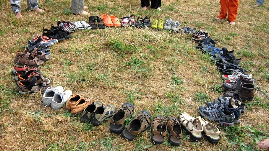 Circle of shoes on dry grass, people standing nearby.