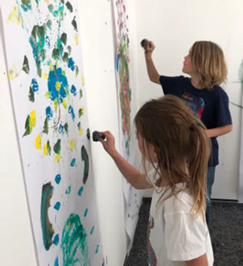 Two children painting colorful art on walls.