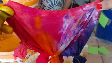 Hands hold colorful, tie-dyed fabric indoors.