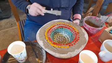 Person erstellt Mosaikschale mit bunten Fliesen.