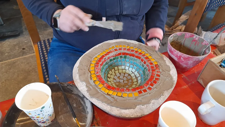 Person crafting mosaic bowl with colorful tiles.