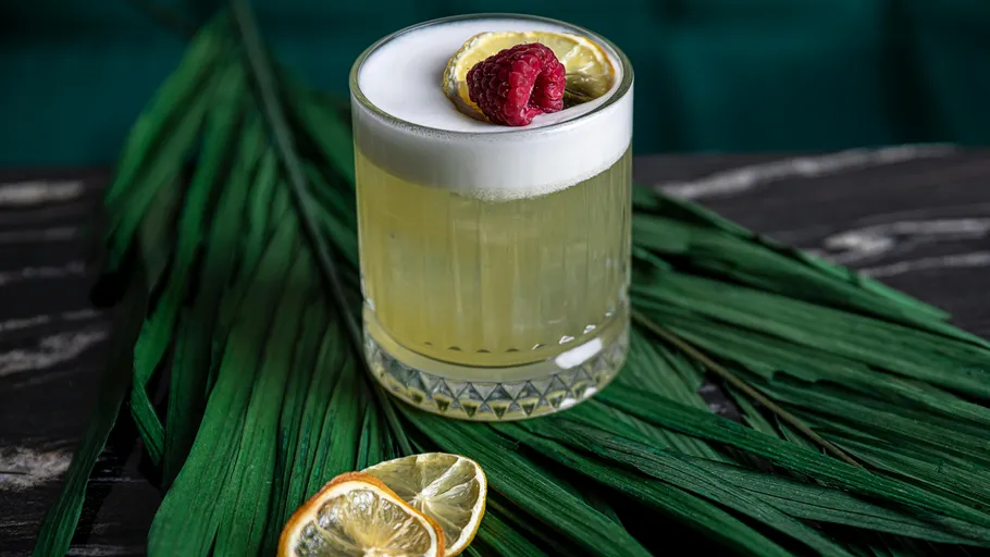 Cocktail mit Schaum und Himbeergarnitur auf Blatt.