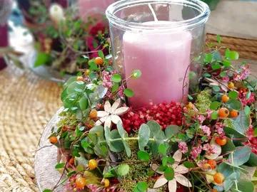 Kerze in dekorativem Blumenkranz auf einem Tisch.