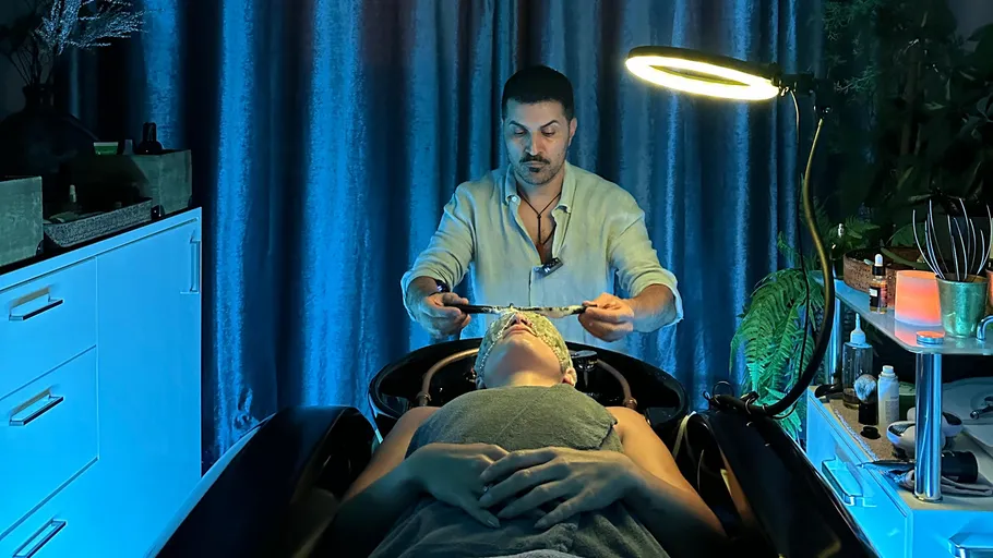 Man performing facial treatment in dim room.