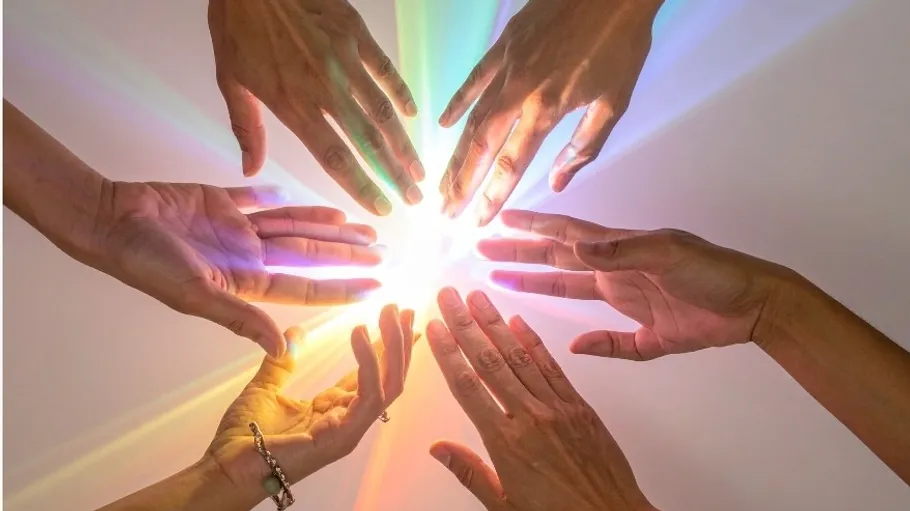 Hands reaching towards bright light, rainbow effect.