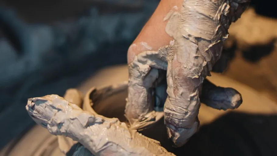 Hands covered in clay shaping pottery.