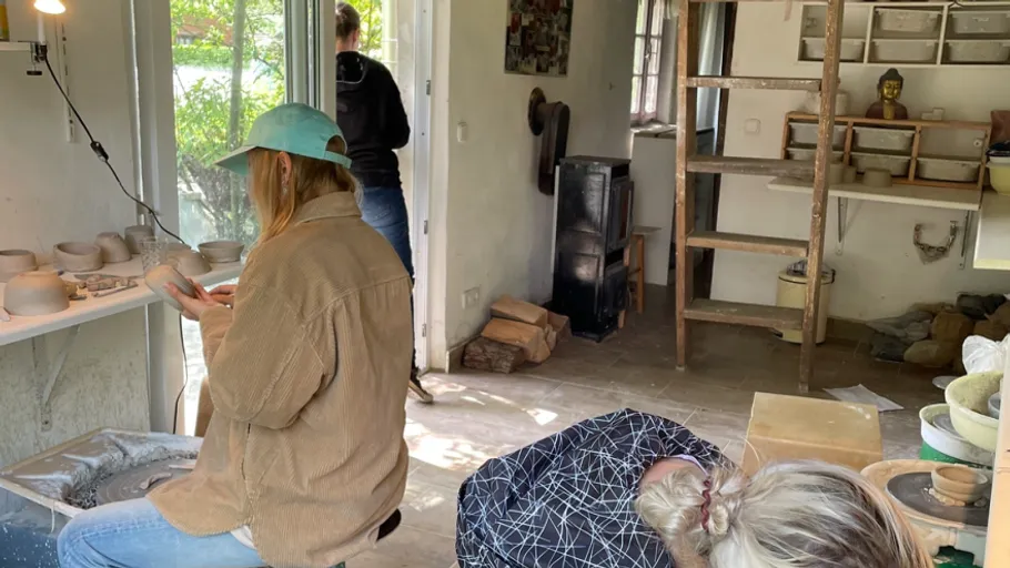 Three people in pottery studio, crafting pots.