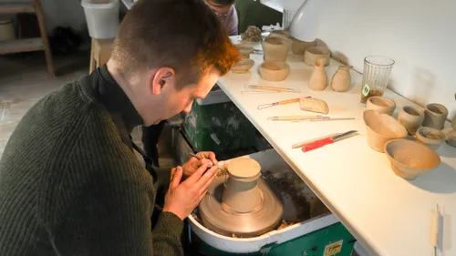 Person crafting pottery on a spinning wheel.