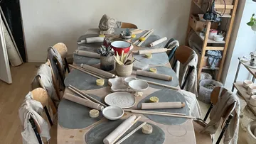 Tisch mit Töpferwerkzeugen, Schalen und Stühlen.