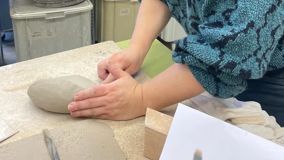 Person shaping clay on a table.