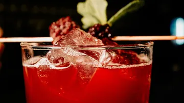 Red cocktail with ice and berry garnish.
