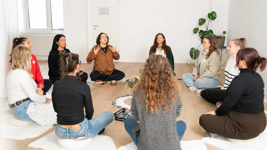 Group sitting in circle meditating indoors.