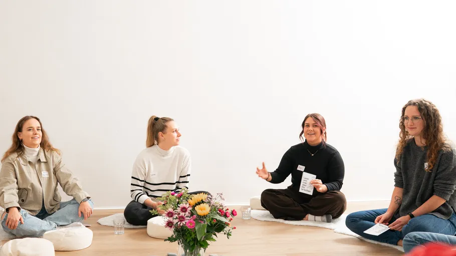 Four women sitting, talking in a bright room.