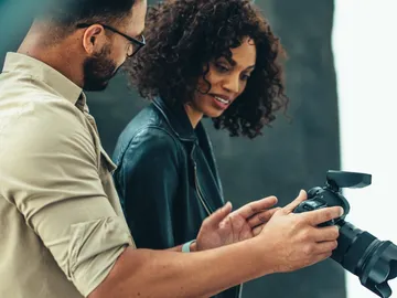 Zwei Personen schauen gemeinsam Fotos auf einer Kamera an.