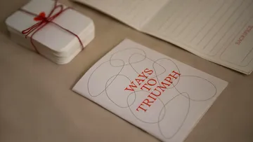Heft mit Titel 'Ways to Triumph' auf Tisch.