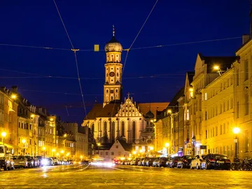 Illuminated square with a church and parked cars.