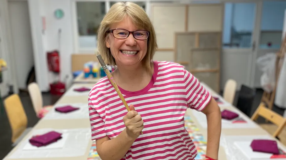 Smiling woman holding a paintbrush indoors.