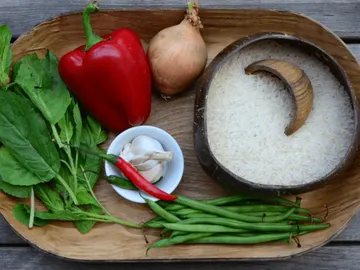 Fresh vegetables and rice arranged on a wooden tray.