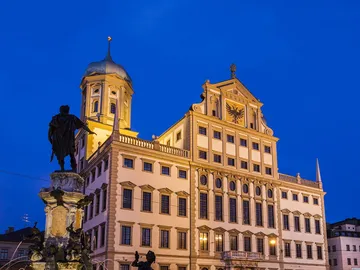 Historic building glows at dusk, statue in the foreground.