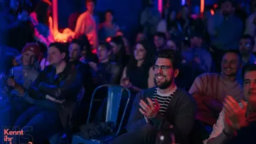 Audience clapping and smiling in a dimly lit venue.