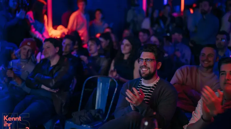 Audience clapping and smiling in a dimly lit venue.
