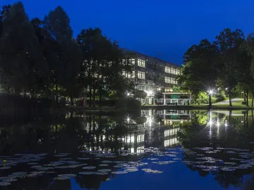 Building reflected in the calm water of a park at night.