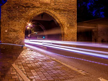 An old stone arch bridge, lights and traffic move fast.