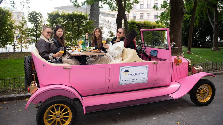 Vier Personen essen in einem rosa Oldtimer.