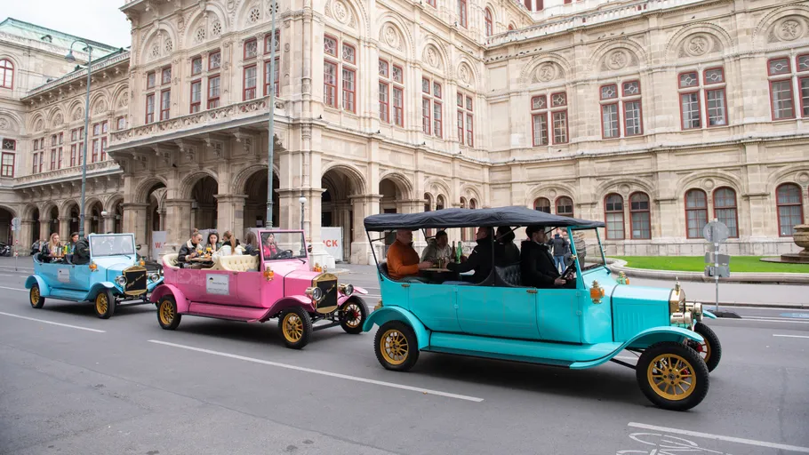 Bunte Oldtimer fahren an historischem Gebäude vorbei.
