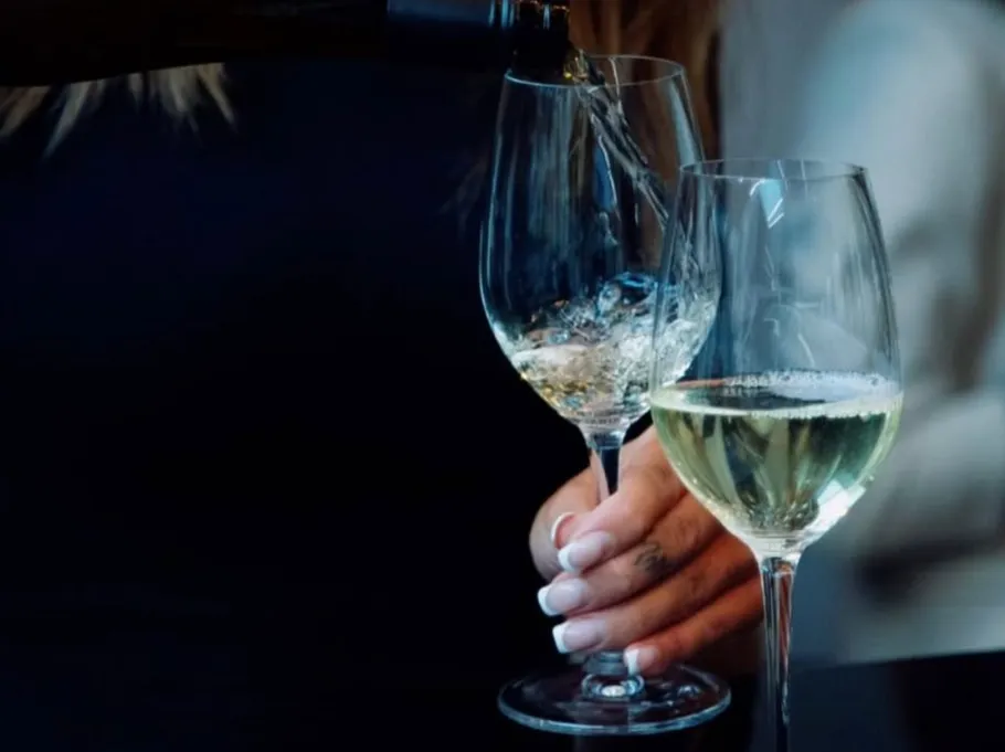 Person pouring white wine into wine glasses.