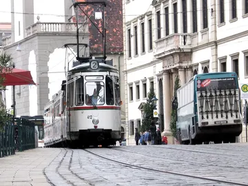 Straßenbahn fährt entlang der Straße, umgeben von Gebäuden.