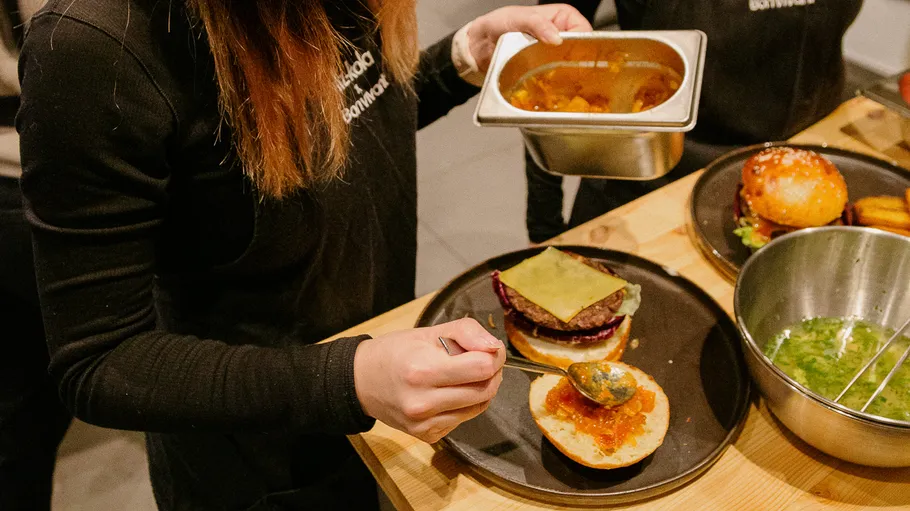 Person fügt Sauce zu einem Burgerbrötchen hinzu.