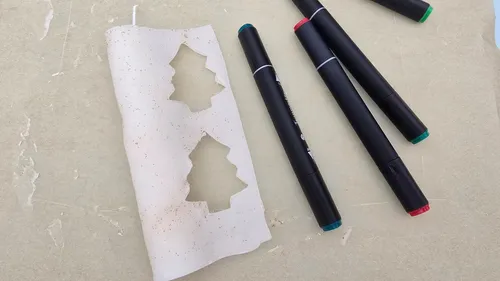 Weihnachtsbaum-Ausschnitte auf Papier neben Stiften.