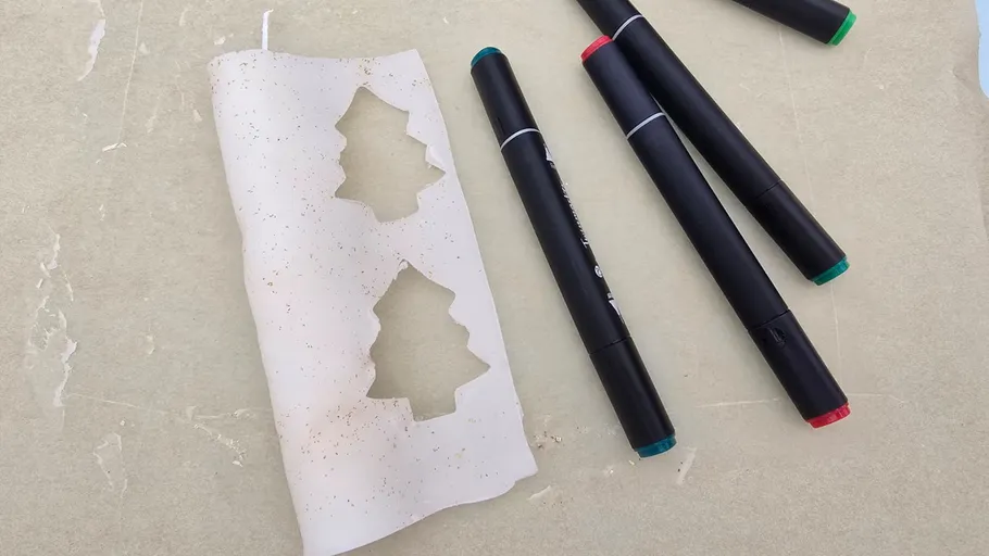 Weihnachtsbaum-Ausschnitte auf Papier neben Stiften.