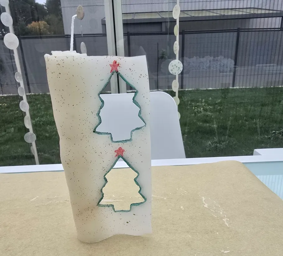 Weiße Kerze mit Baum-Formen auf Tisch.