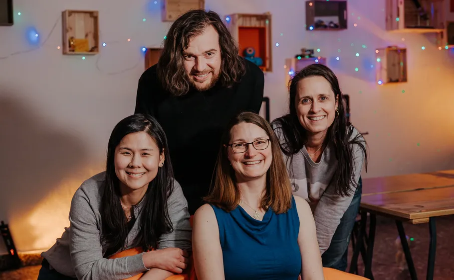Four smiling people indoors with colorful lights.