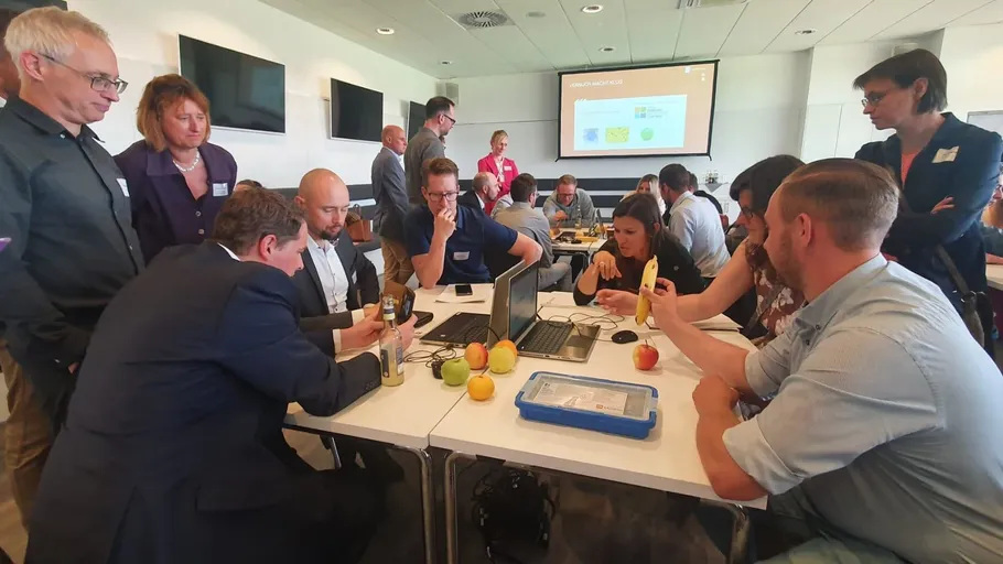 People examining fruit and laptops in meeting room.