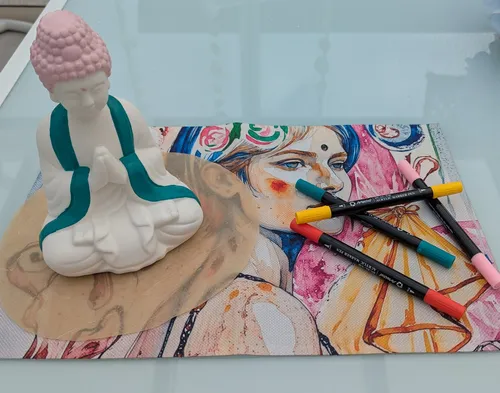 Buddha statue, art markers, colorful portrait on table.