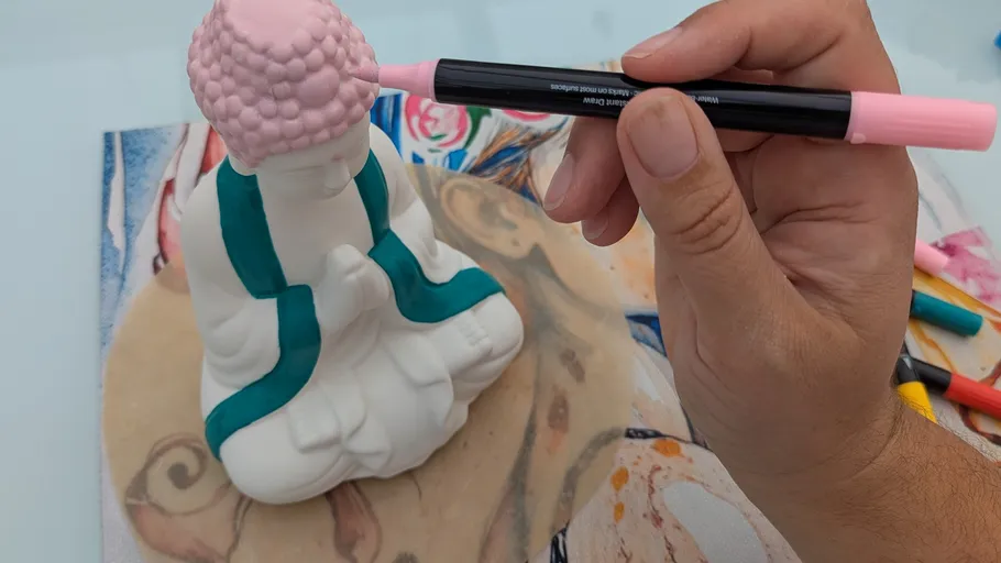 Hand coloring a small Buddha statue with markers.