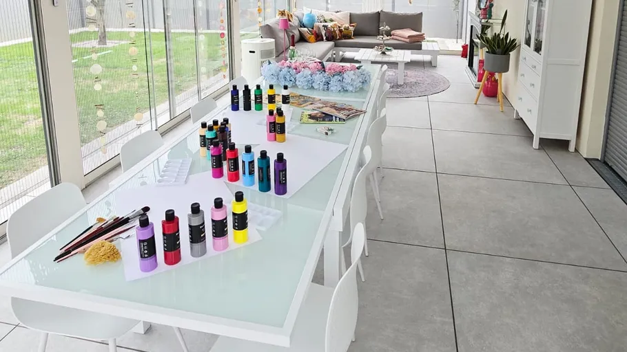 Art supplies on long table in sunroom.