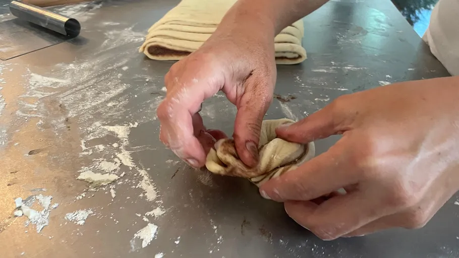Hands shaping dough on a floured surface.