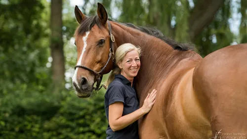 Woman smiling beside large brown horse outdoors.