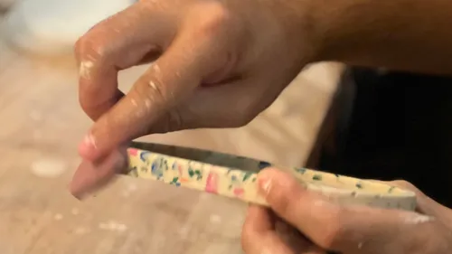 Hands shaping clay tile on worktable.