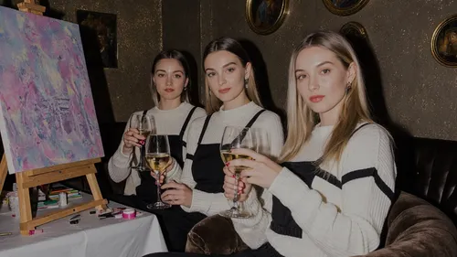 Drei Frauen mit Wein neben Gemälde.