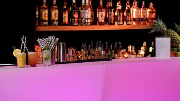 Cocktail bar with pink lighting and bottles.