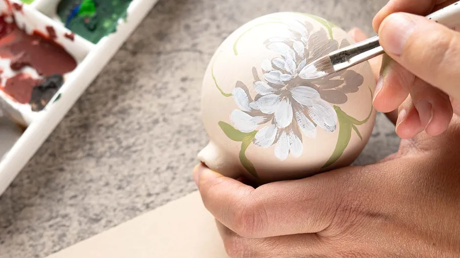 Person painting floral design on a ceramic object.