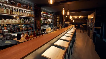 Empty bar with wooden stools, dim lighting.